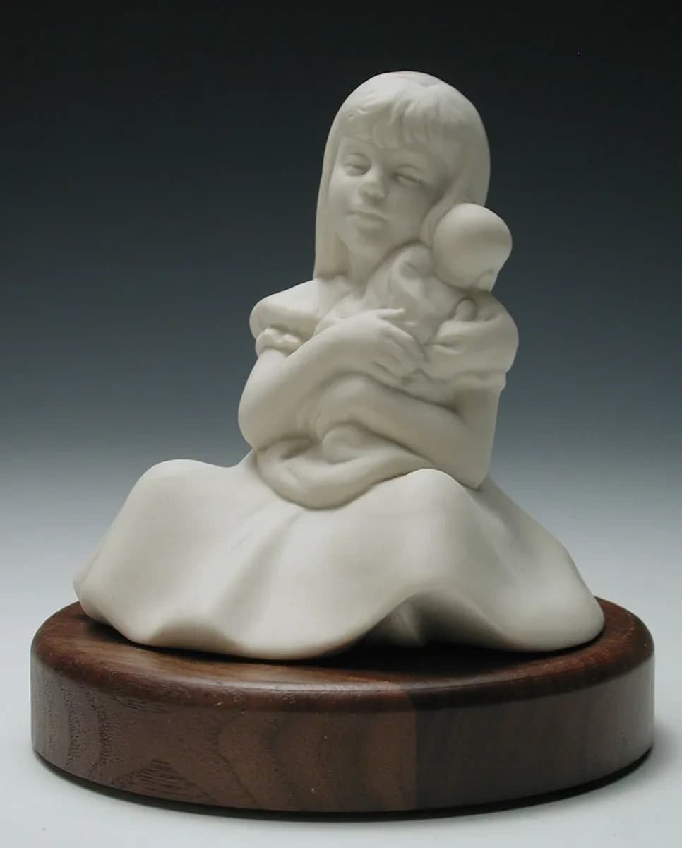 White porcelain figurine of a young girl sitting in a full skirt, hugging a doll to her cheek, on a round timber base